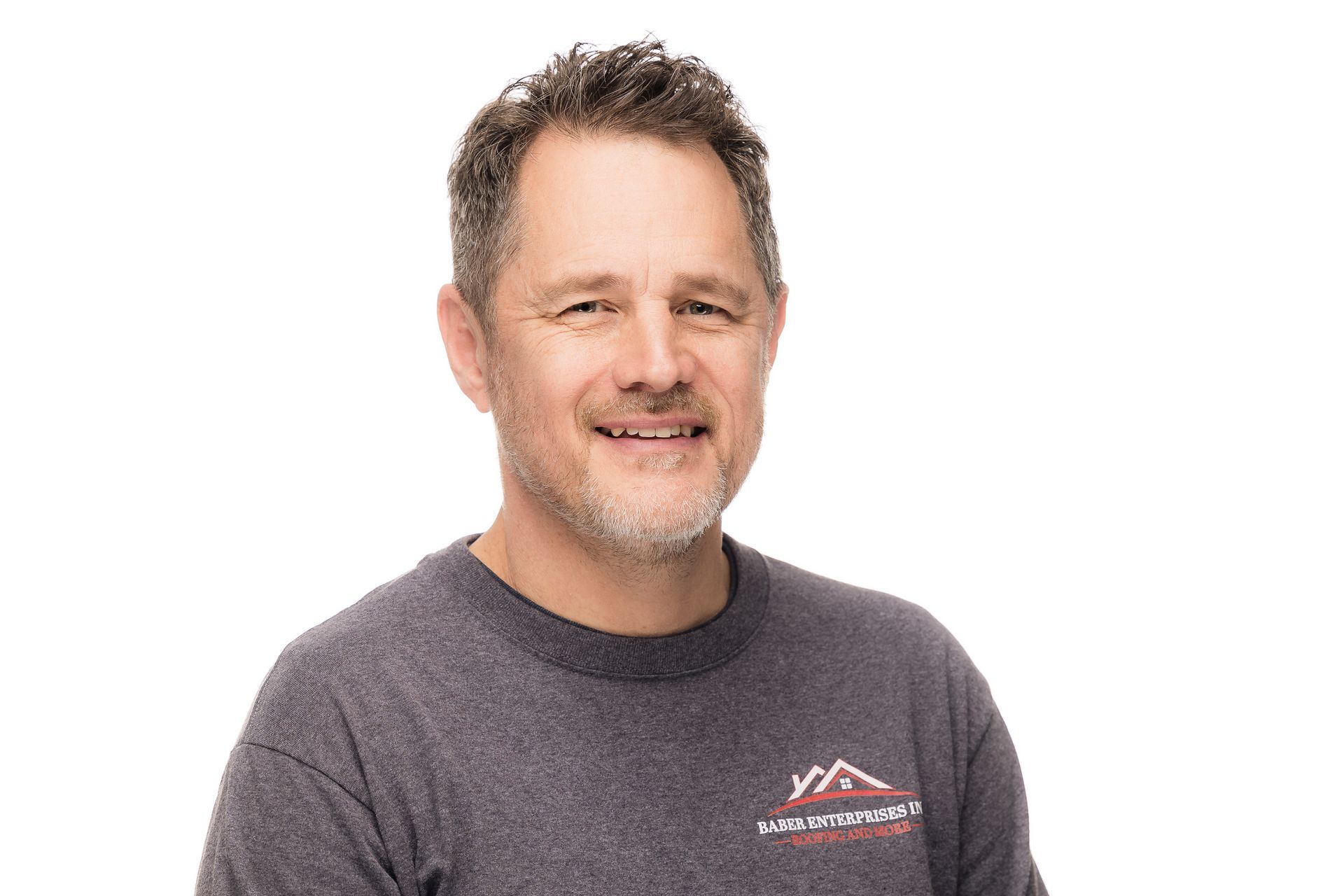 A man with a beard is wearing a gray shirt and smiling.