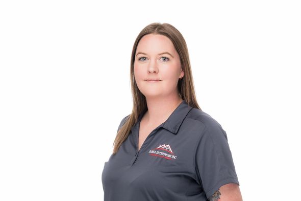 A woman in a gray shirt is standing in front of a white background.