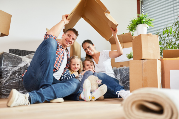 A family is sitting on the floor under a cardboard house.