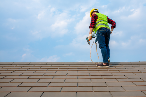 A man is standing on top of a roof holding a hammer.