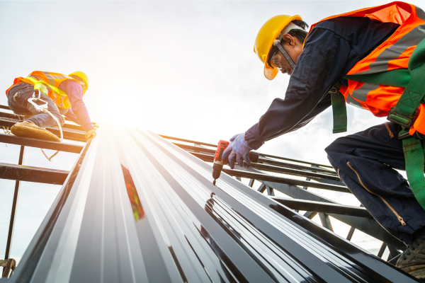 Two construction workers are working on the roof of a building.