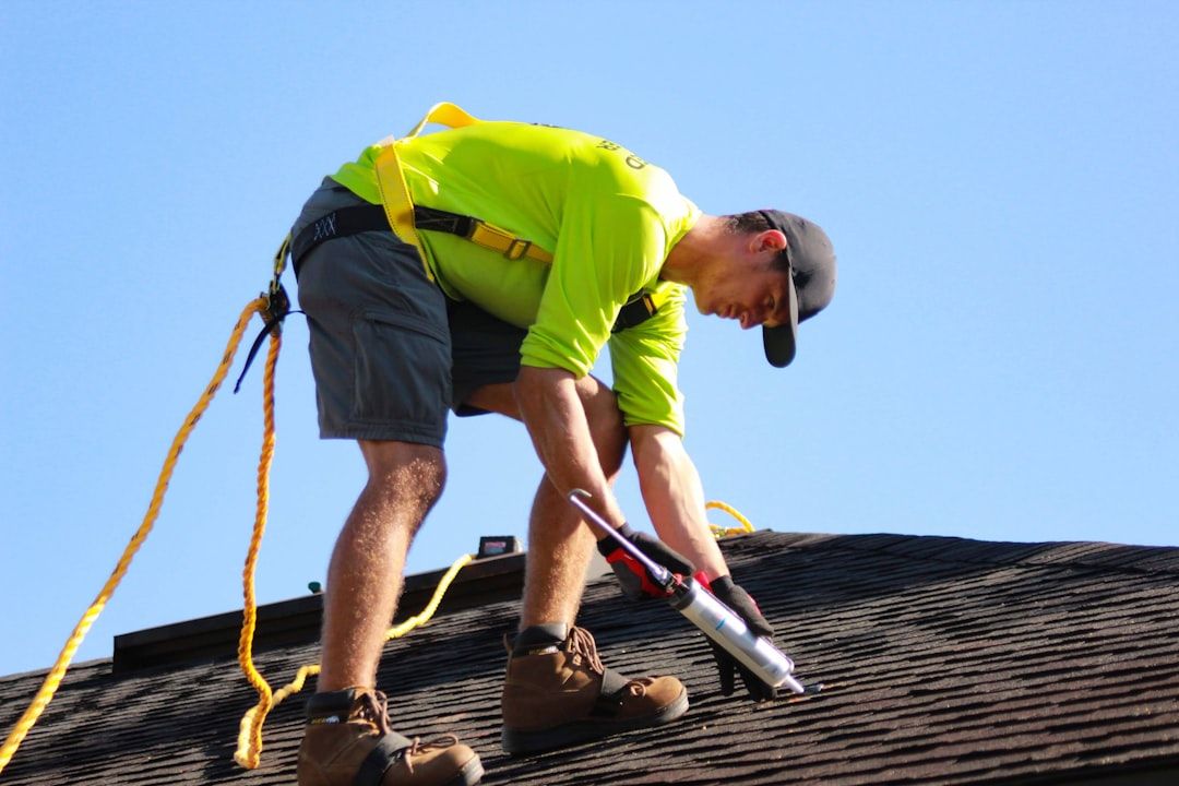 A man is kneeling on a roof holding a bottle of glue.