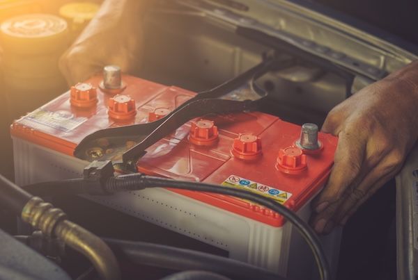 Hands installing a car battery in an engine compartment.