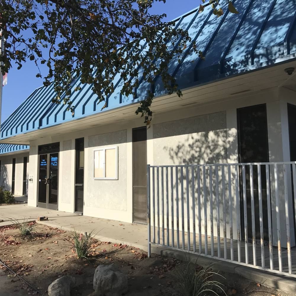 A white building with a blue roof and a fence in front of it.