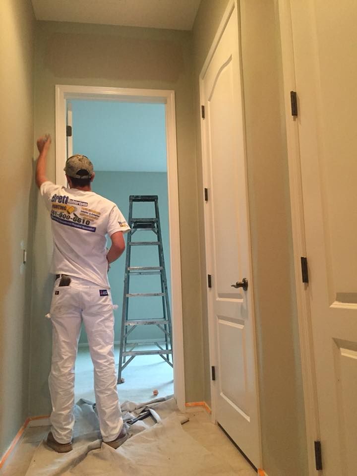 A man is painting a door in a hallway next to a ladder.