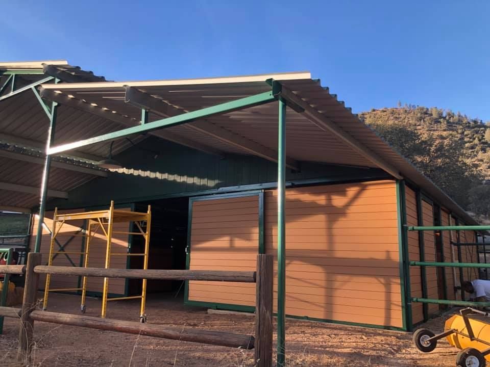 A horse barn with a green roof and a wooden fence.