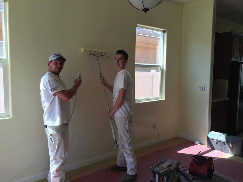 Two men are painting a wall in a room.