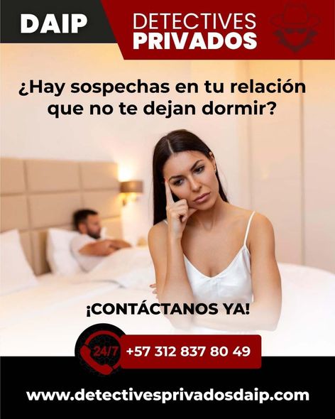 Una mujer de semblante serio está sentada en una cama mientras su pareja yace detrás de ella.