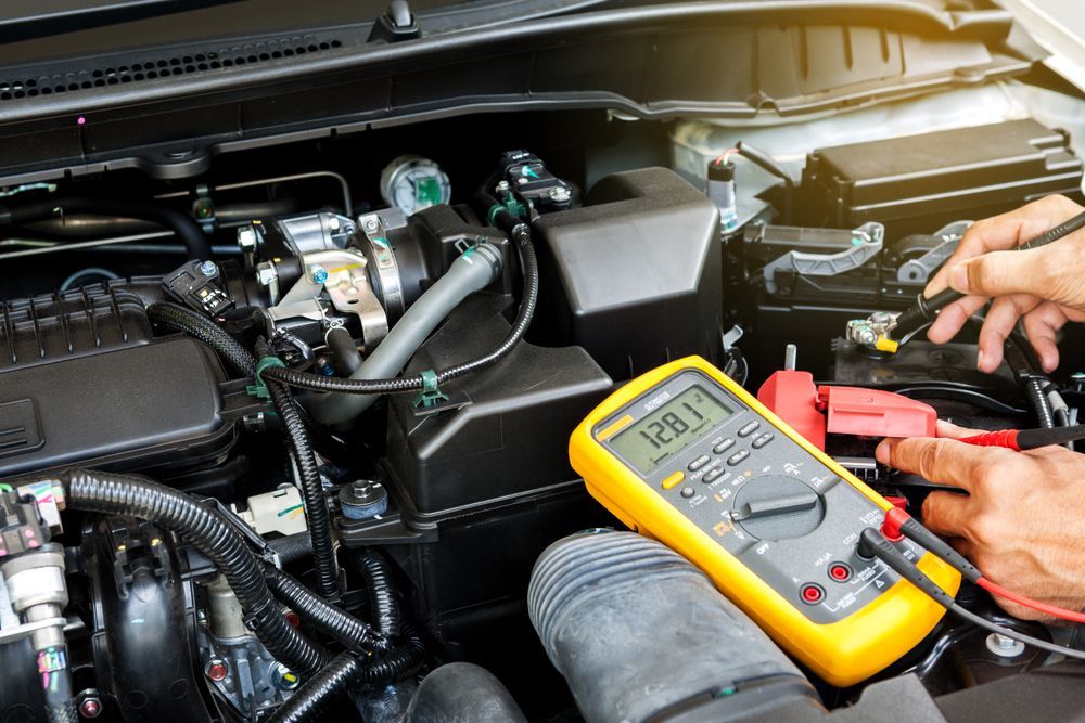 Car engine being tested with a multimeter. Hands connect probes to battery terminals, displaying a voltage reading — Drinnan's Diesel & Automotive Repairs In Gladstone Central, QLD