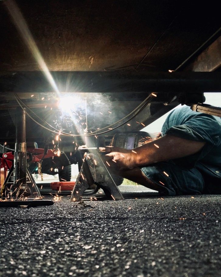A Man is Welding Under a Car on the Ground — Drinnan's Diesel & Automotive Repairs In Gladstone Central, QLD