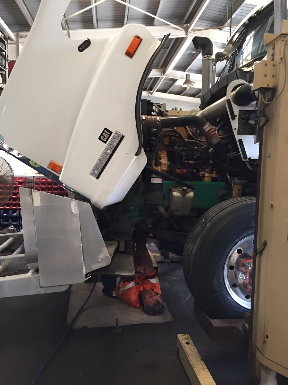 A Man is Laying Under the Hood of a Truck in a Garage — Drinnan's Diesel & Automotive Repairs In Gladstone Central, QLD