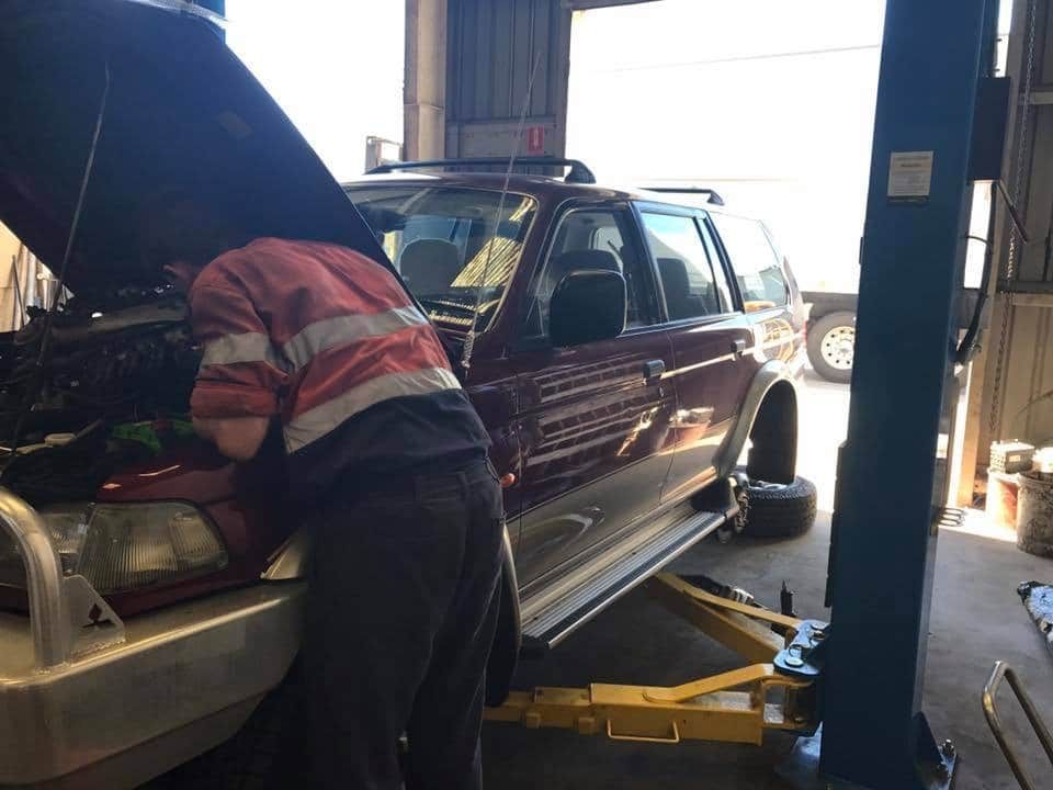 A Man is Working on a Car in a Garage With the Hood Open — Drinnan's Diesel & Automotive Repairs In Gladstone Central, QLD