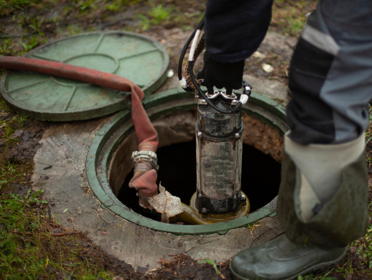 Person pumping out a septic tank, using a pump and hose.