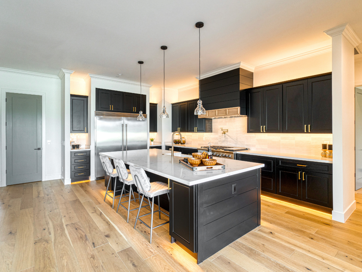 Modern kitchen with black cabinets, white island, wood floors, and warm lighting.