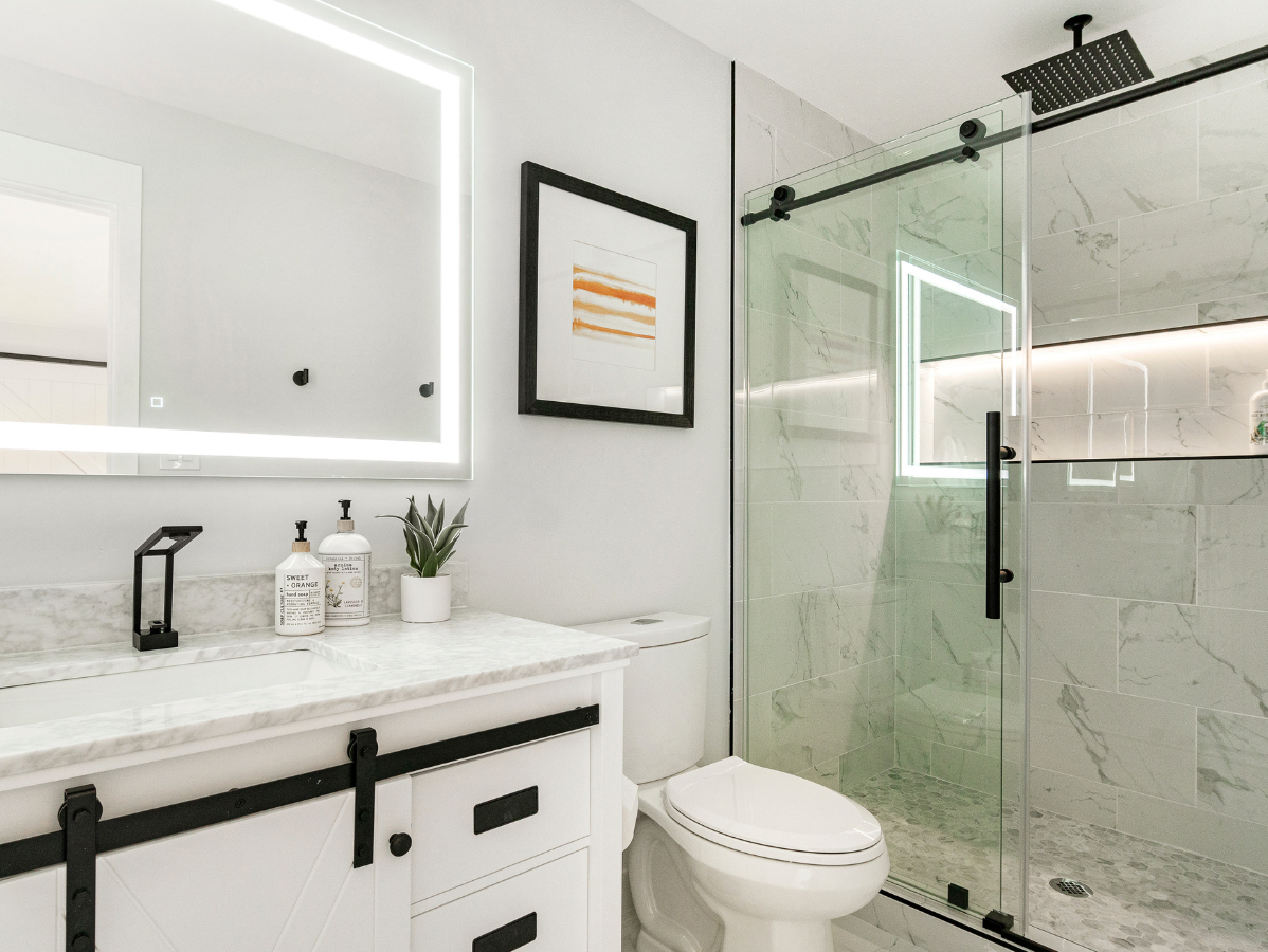 White bathroom with marble shower, vanity with black hardware, and a framed art piece.