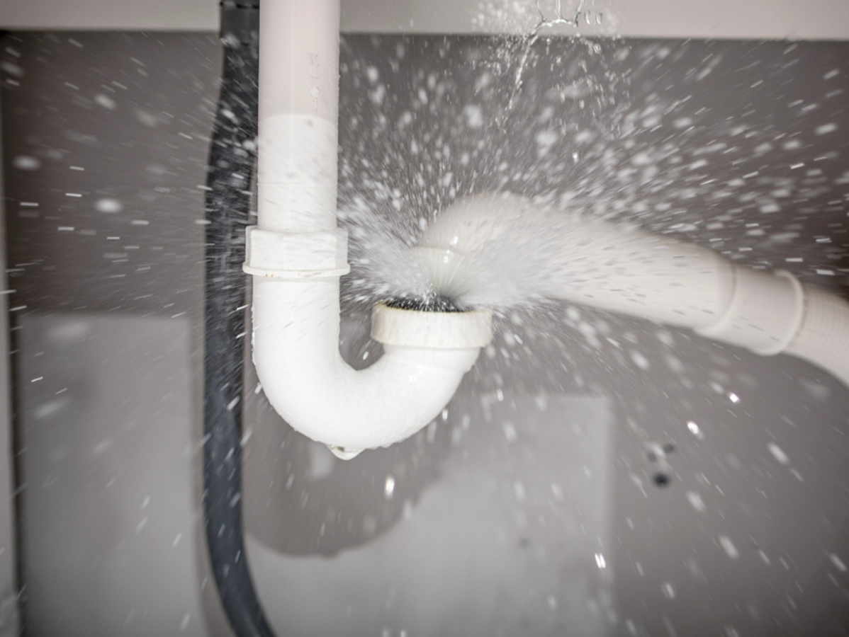 White plumbing pipes leaking water under a sink.