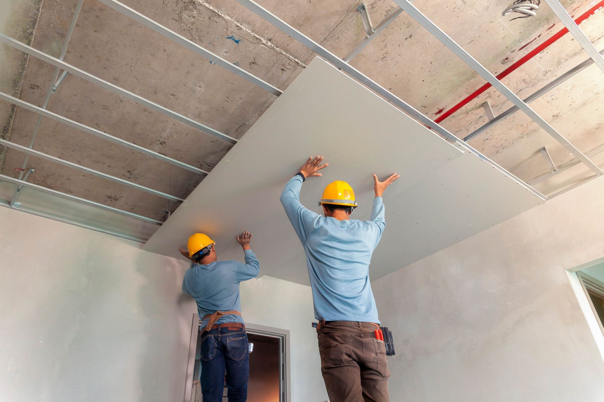 Two construction workers are installing a ceiling in a room.