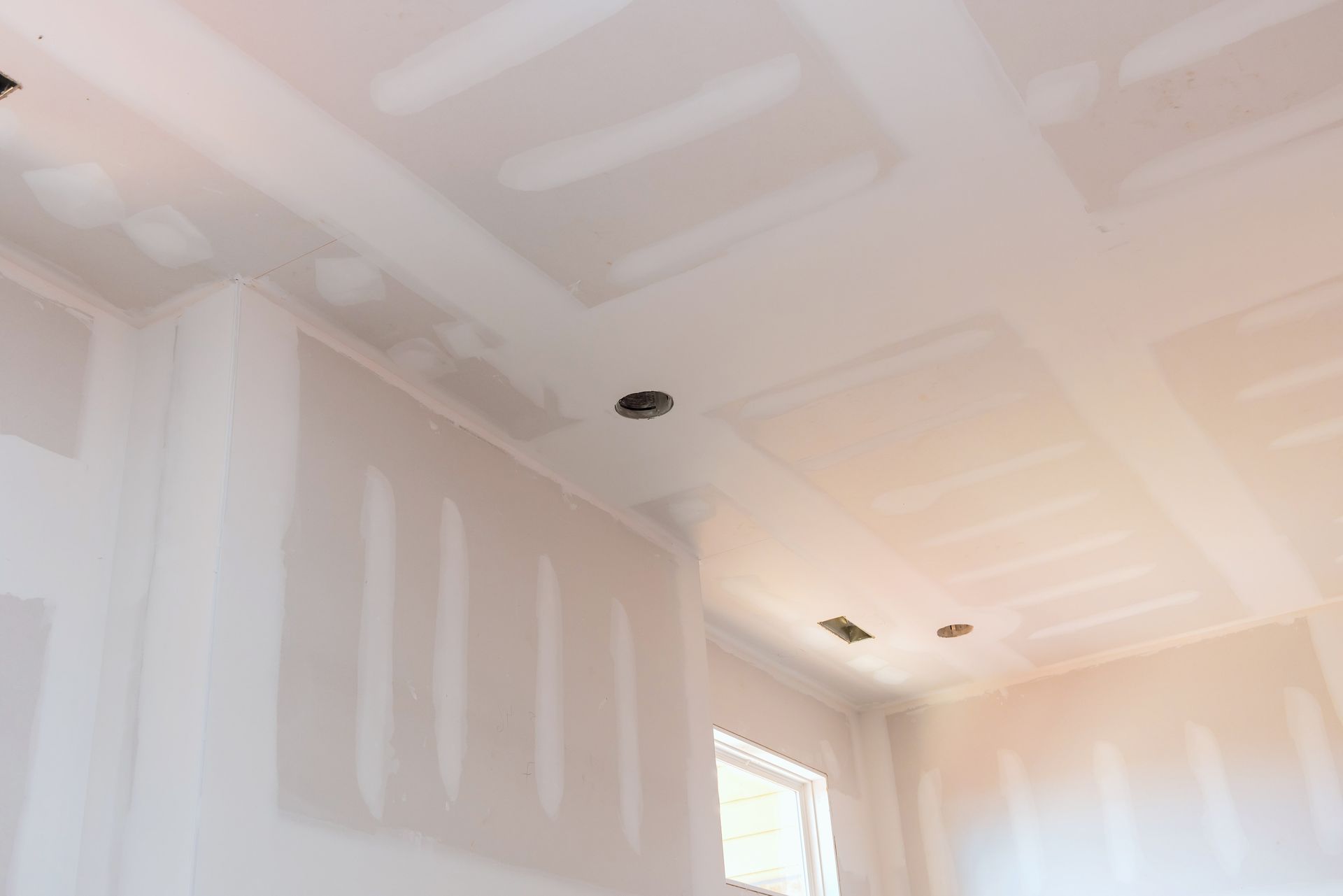 A room with a ceiling that is covered in drywall and a window.
