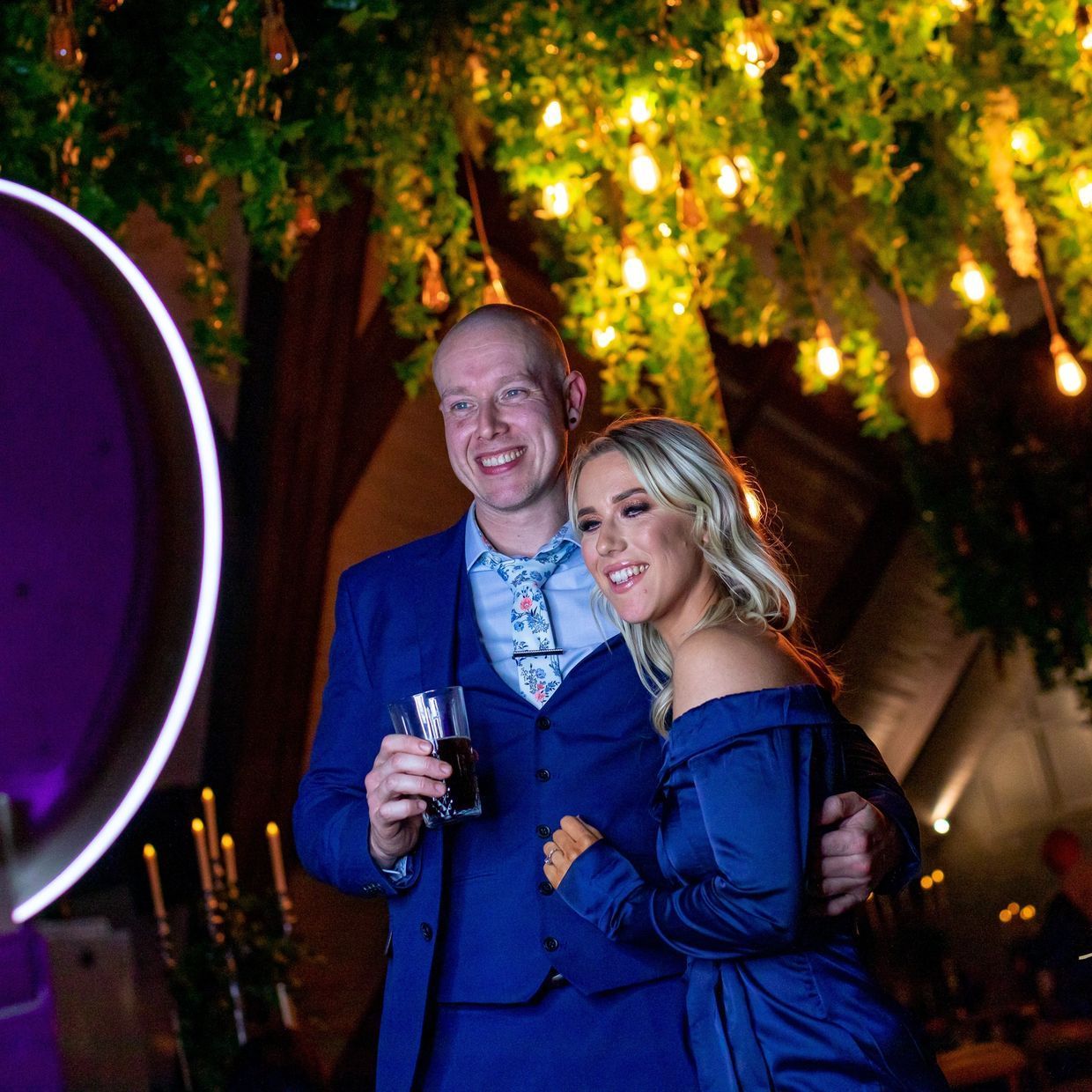 A man in a suit and tie is holding a glass of wine next to a woman in a blue dress.