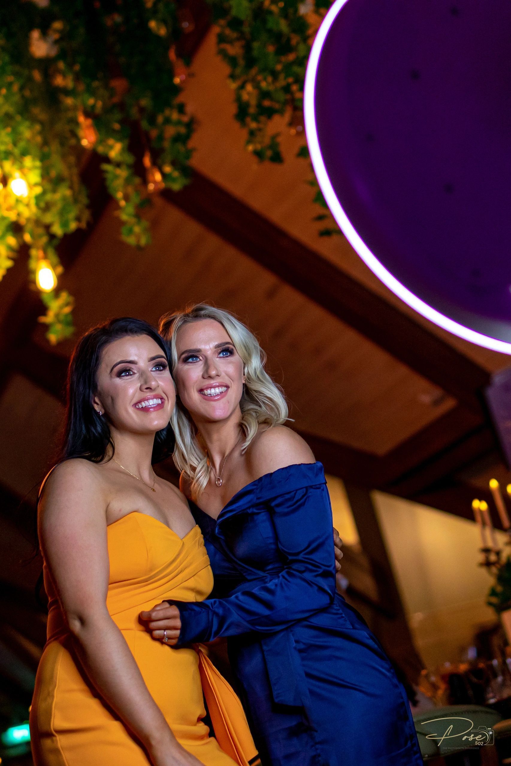Two women are posing for a picture together in front of a purple circle.