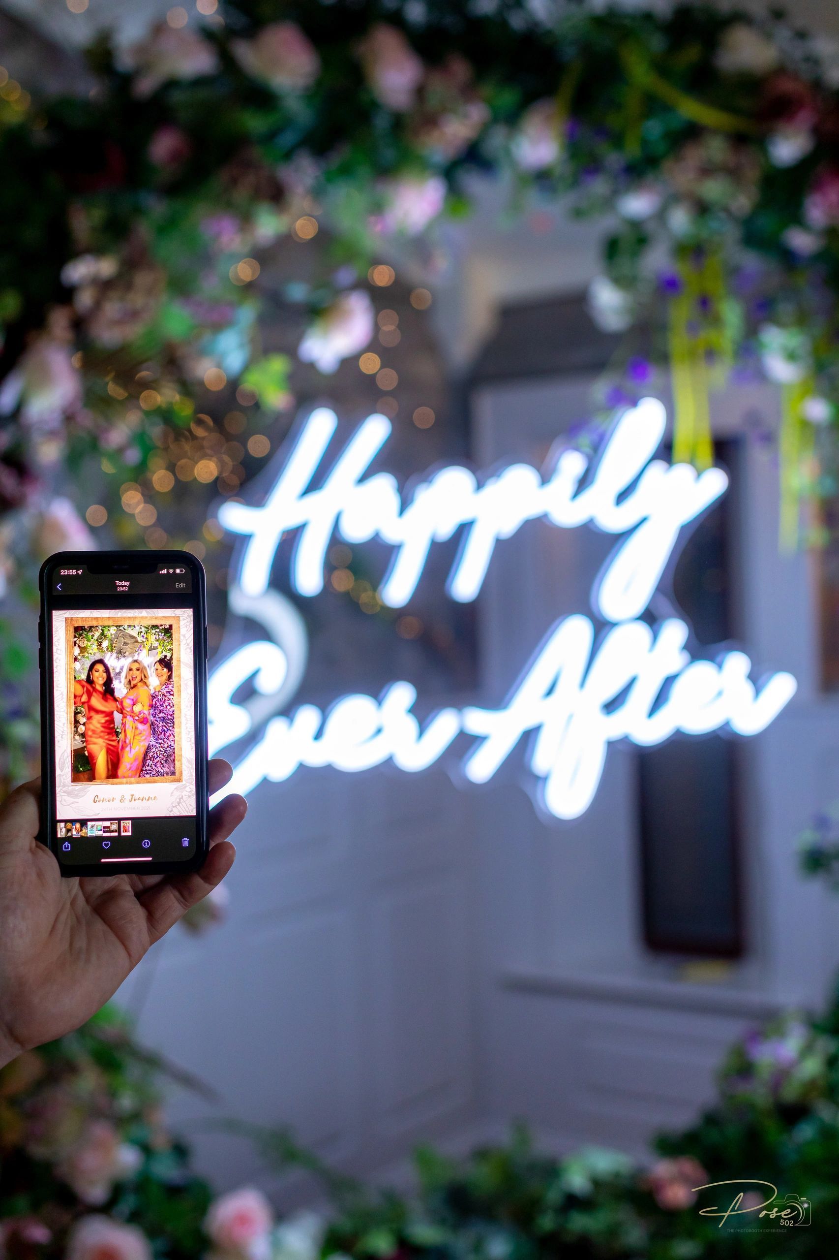 A person is holding a cell phone in front of a neon sign that says `` happily ever after ''.