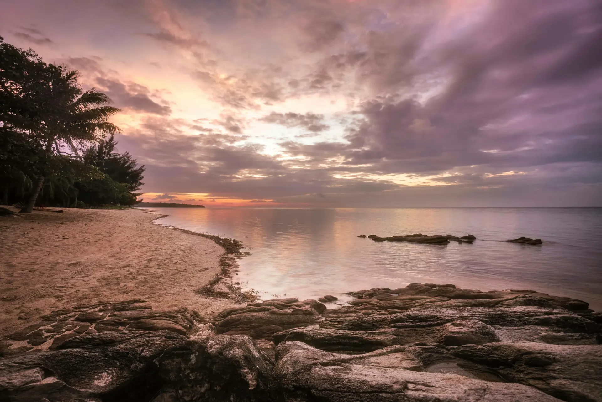 A sunset over a beach with rocks and trees