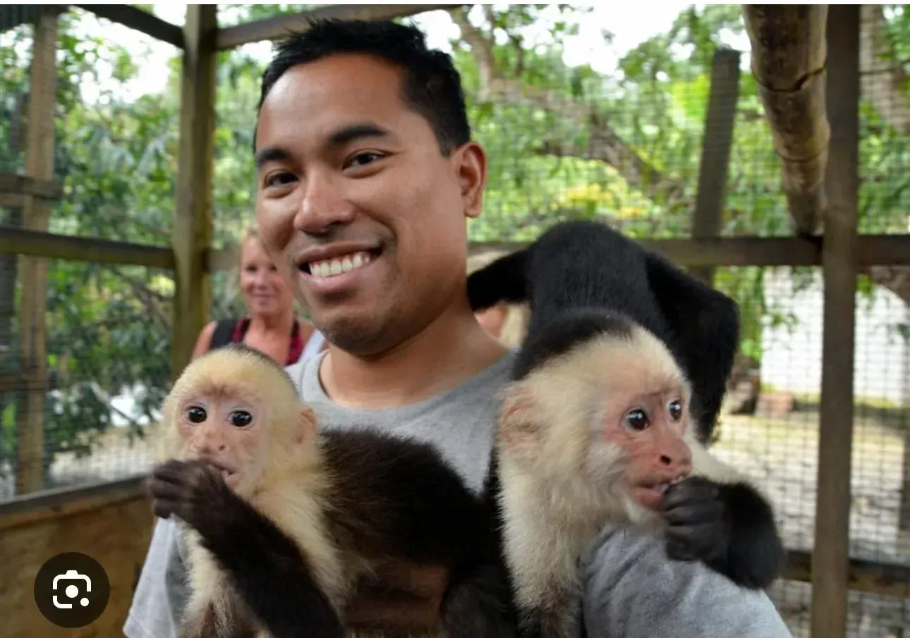 A man is holding two monkeys in his arms and smiling