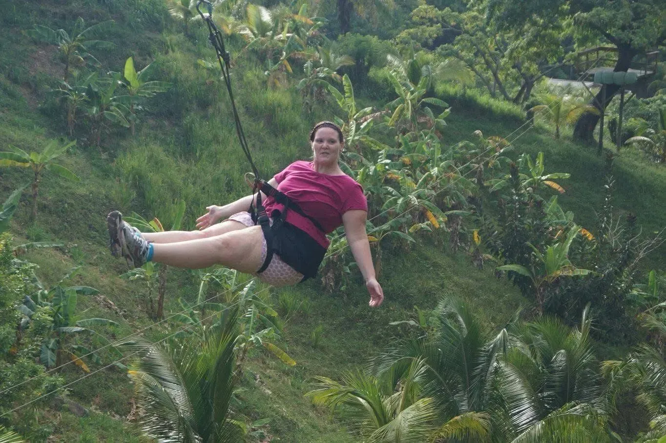 A woman is flying through the air on a zip line in the jungle.