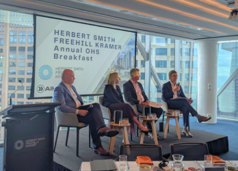 Panel discussion: Herbert Smith Freehill Kramer Annual OHS Breakfast, four people seated on stage, city backdrop.