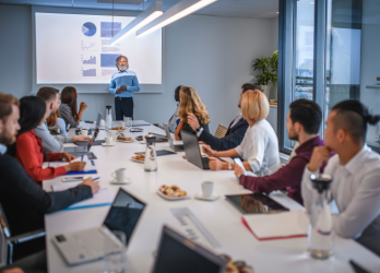 group of people sitting at a boardroom table, man is presenting slides