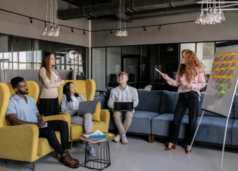 Small team meeting in a modern office lounge, with one person presenting beside a flip chart.