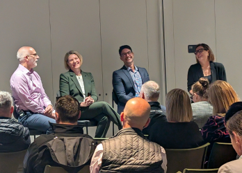 Panel discussion with four speakers seated before an audience in a conference room