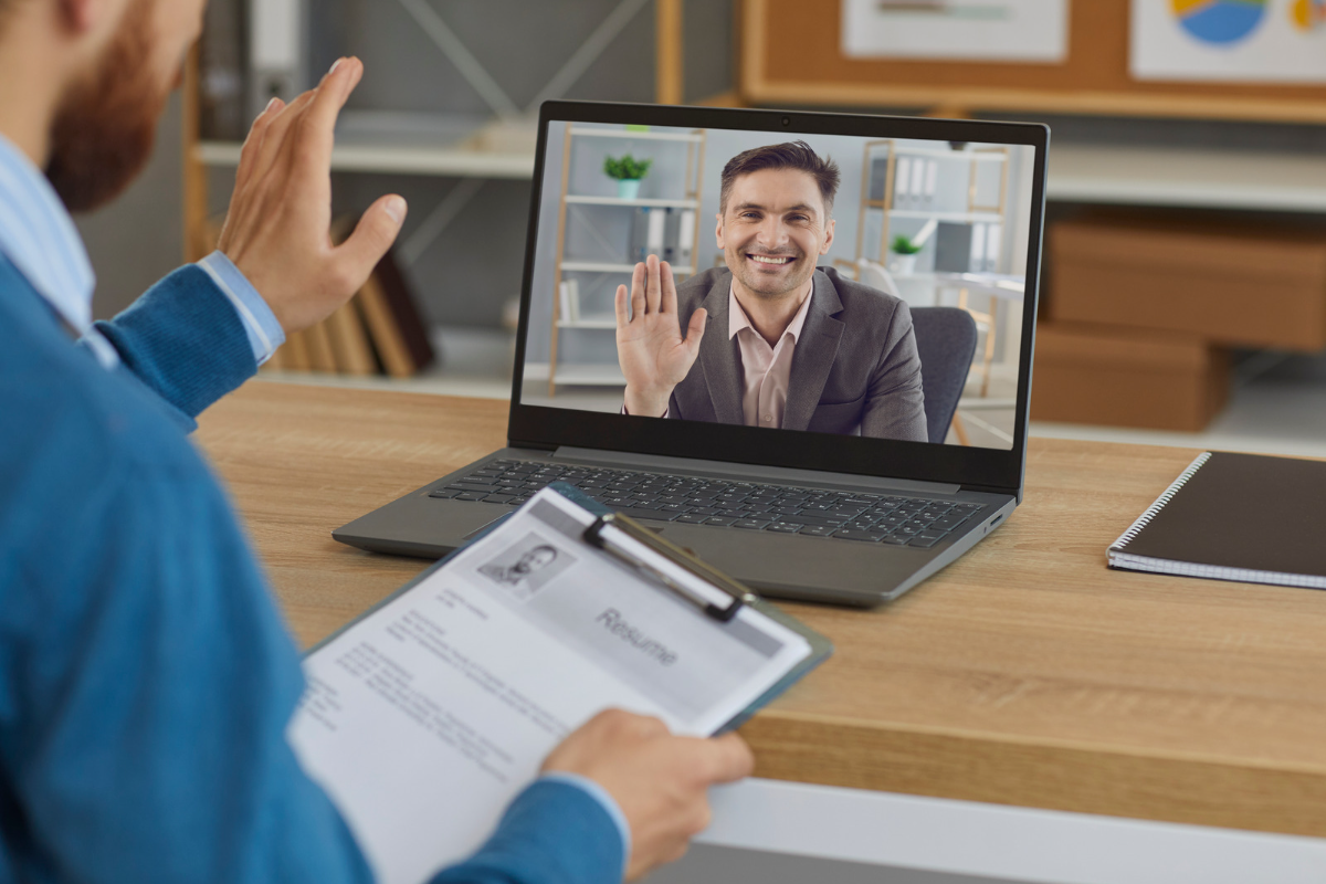 man holding a printed resume waving at man through video conferencing technology