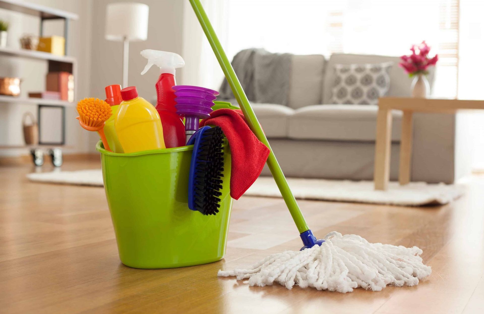 A green bucket filled with cleaning supplies and a mop in a living room.