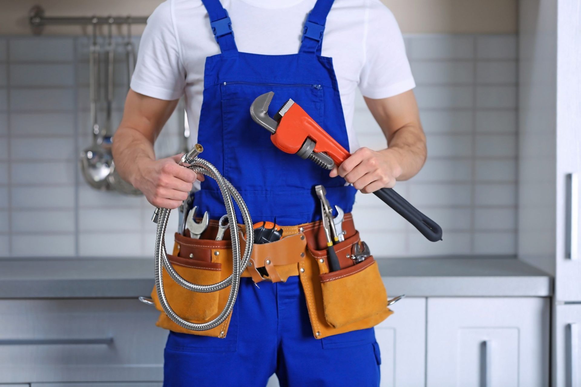 A handyman is holding a wrench and a hose for providing handyman services in NYC.