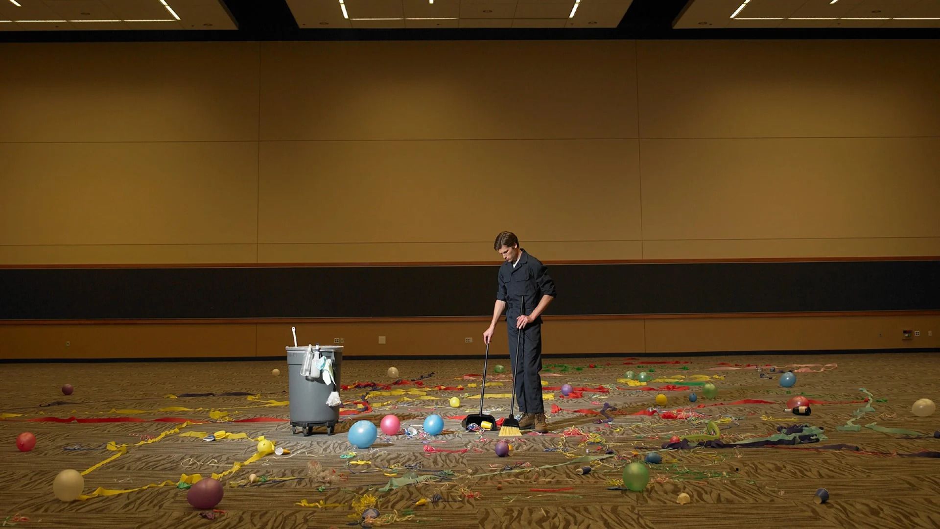 A man is cleaning a messy room with balloons and confetti.