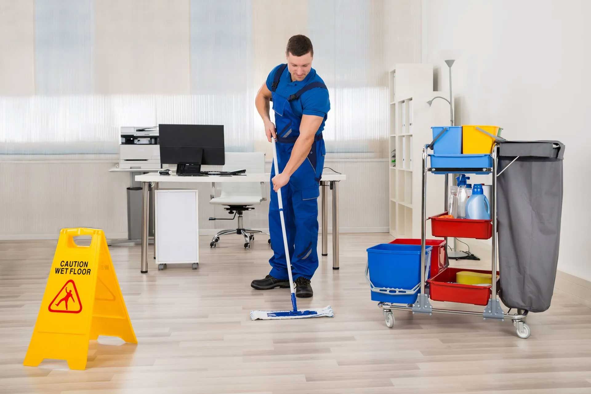 A man from dll ofiice cleaners is cleaning the floor of an office with a mop.