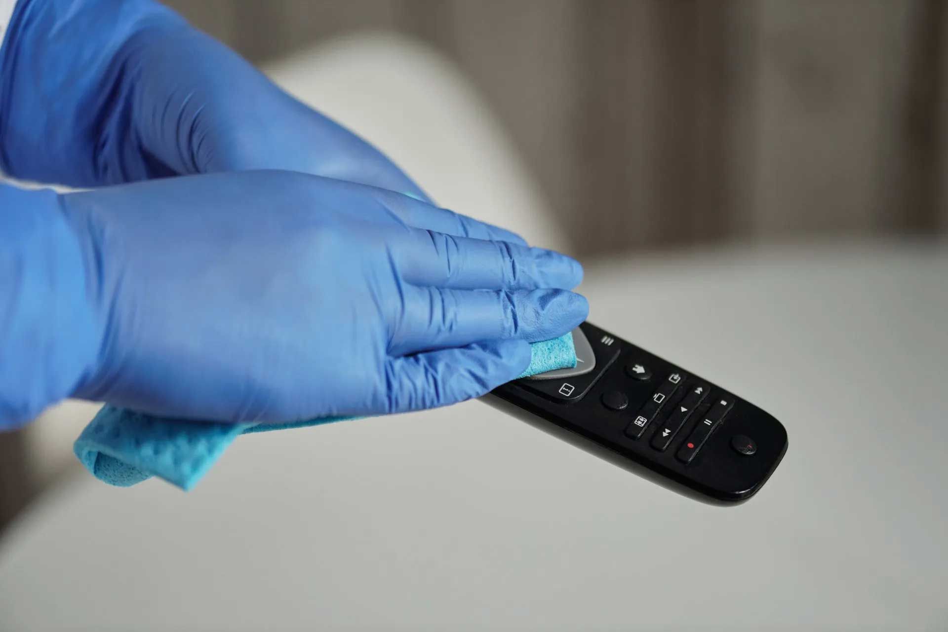 a person wearing blue gloves is cleaning a remote control with a cloth .