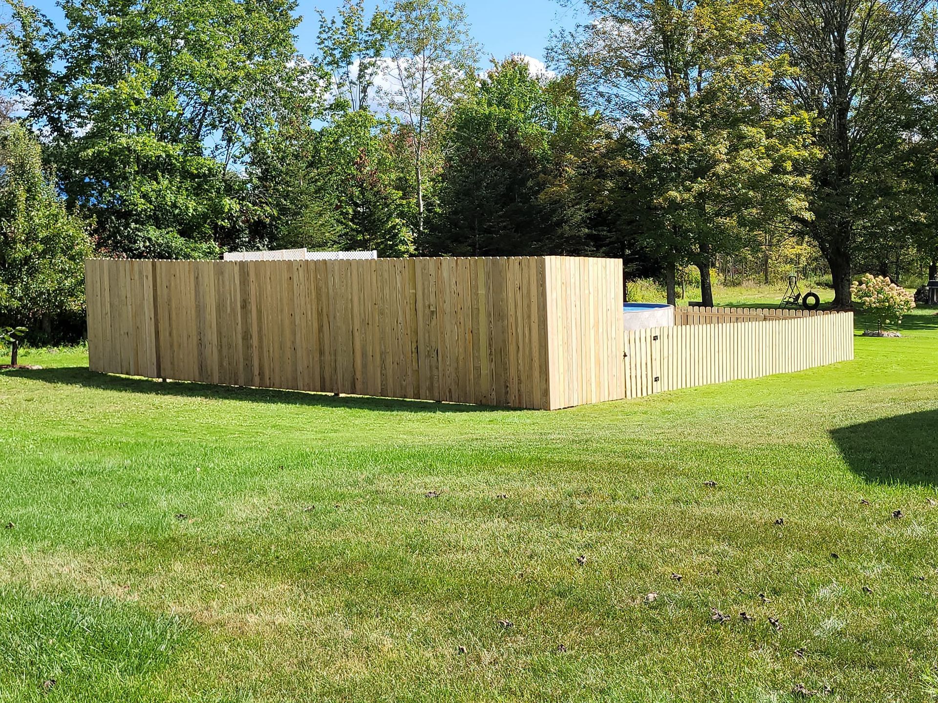 Wooden fence surrounding a pool in a grassy yard, trees in background.