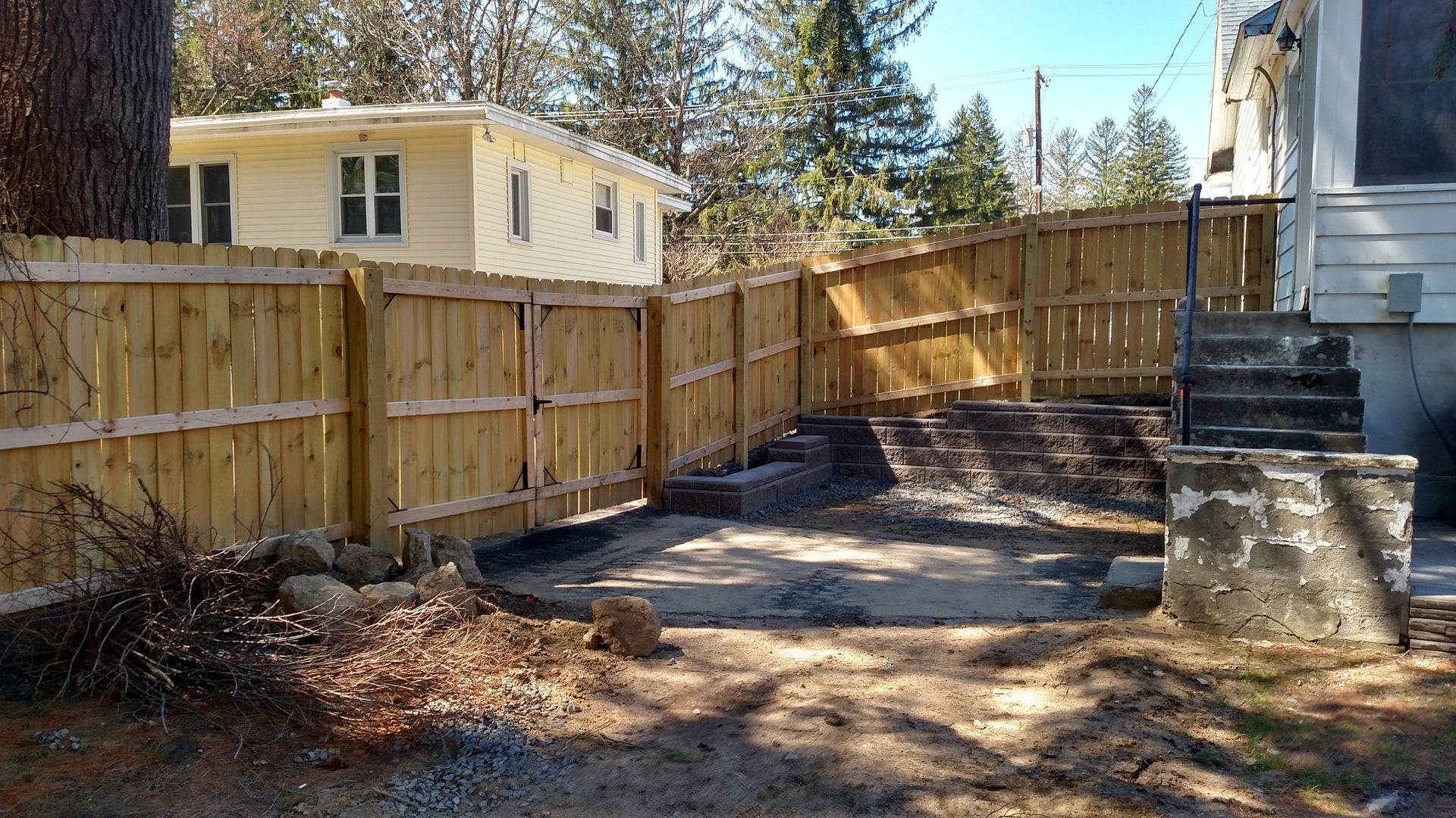 Wooden fence around a yard with a small building on the left and stairs to a building on the right.