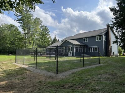 Black fenced-in yard around a house with blue siding, a large lawn, and a partly cloudy sky.