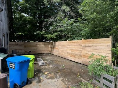 Backyard with wooden fence, trash bins, and a small garden.