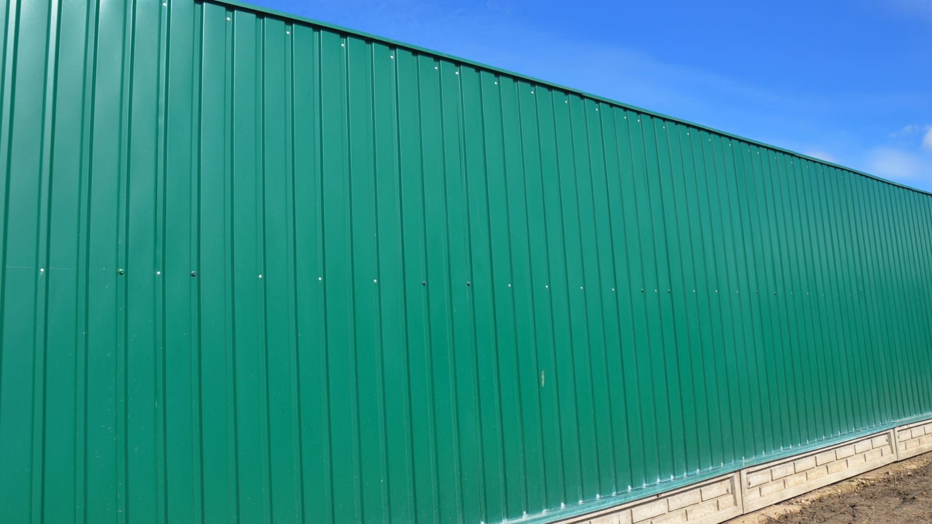 Green corrugated metal fence against a blue sky.