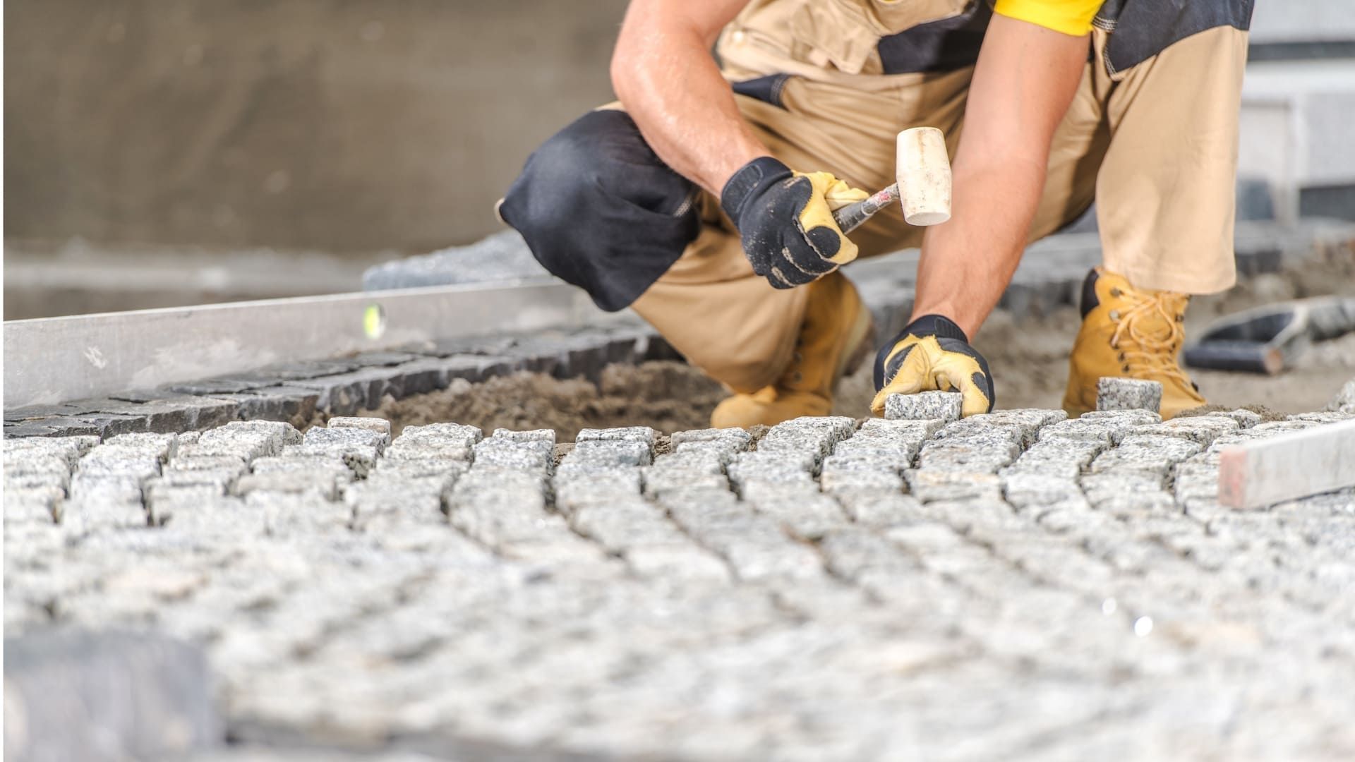 Construction worker kneeling, using a hammer to set paving stones.