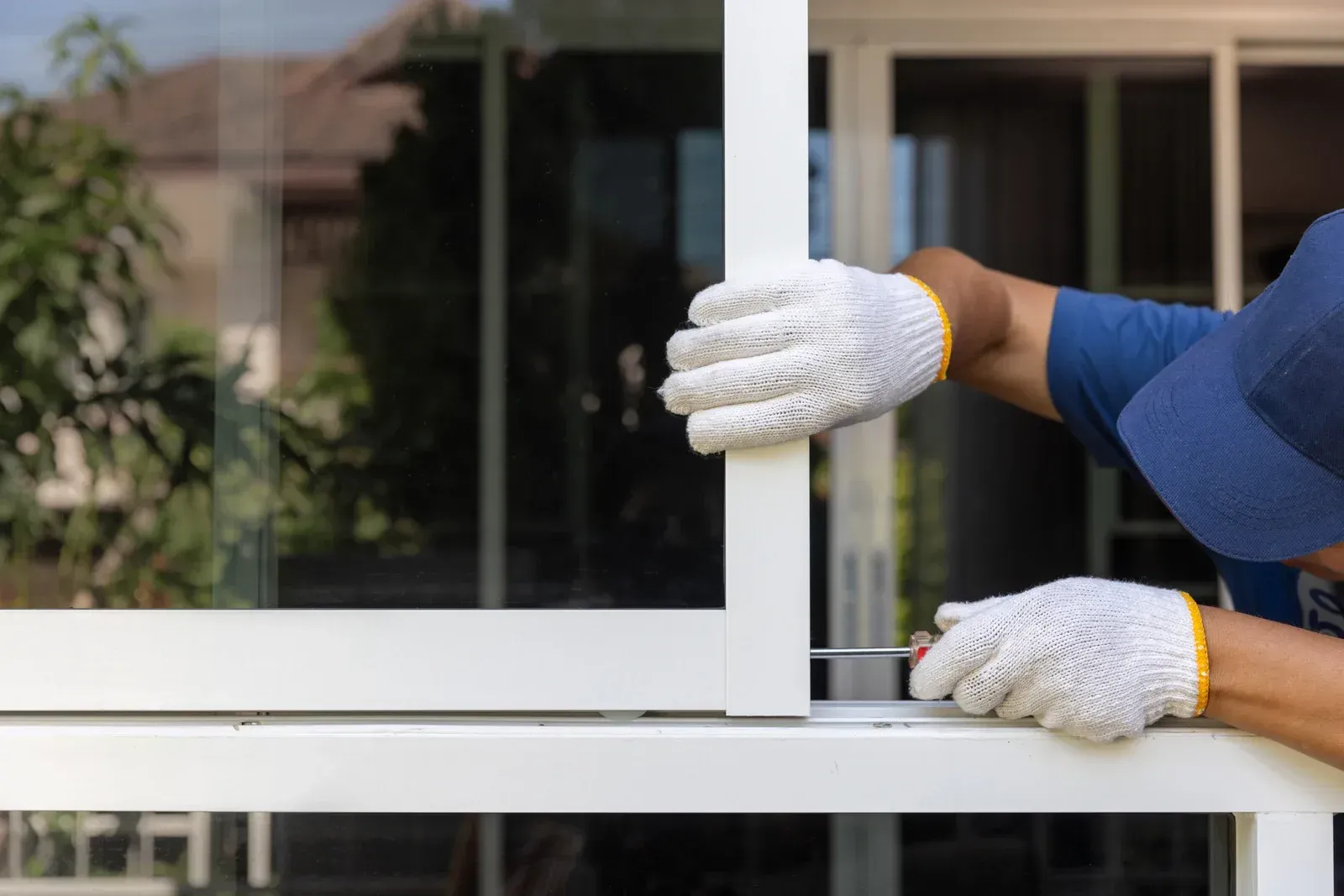 Person in gloves sliding a white framed window or door, outdoor setting.