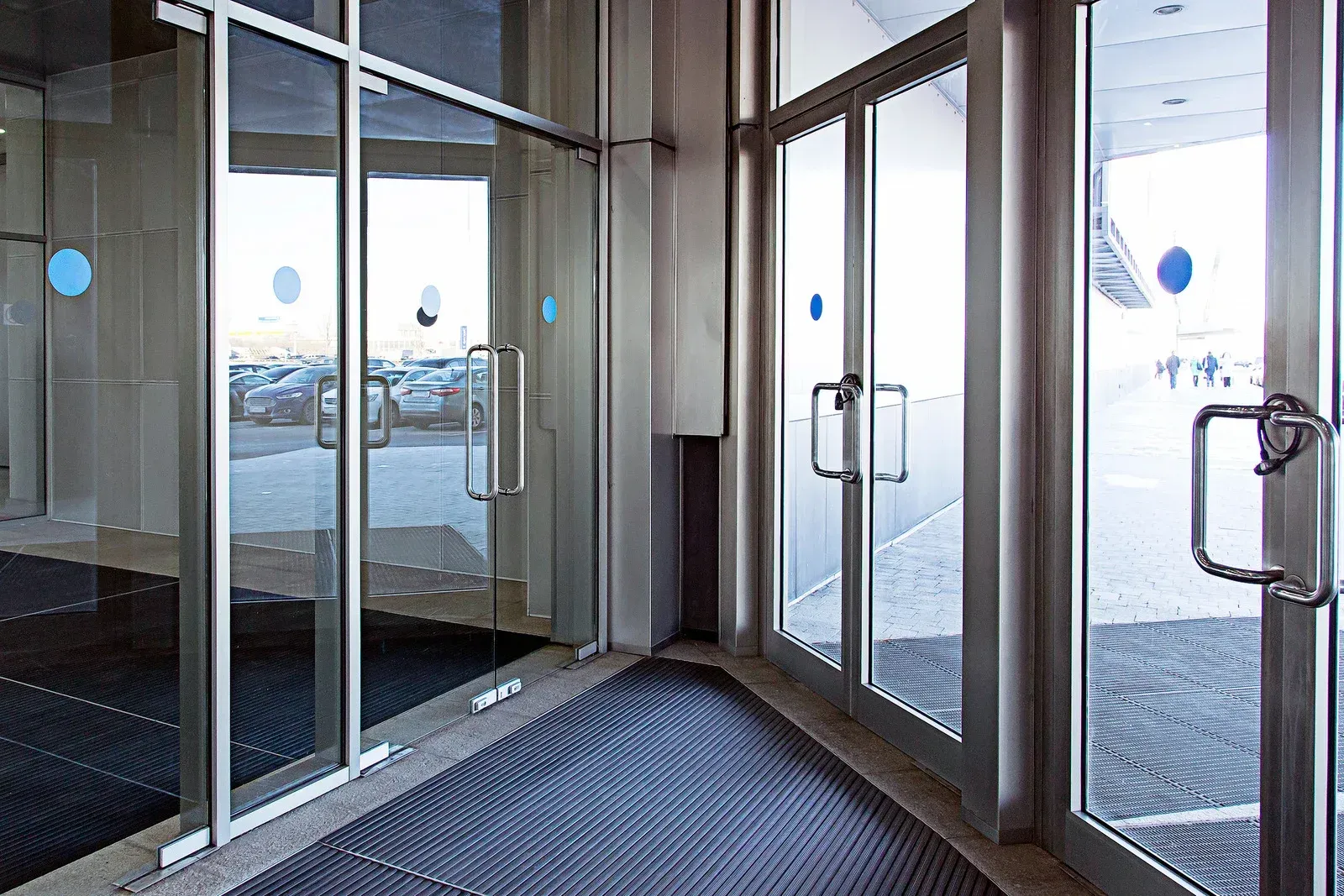 Glass doors with silver frames, blue circles, and metal handles. Entrance to a building with a blue doormat.