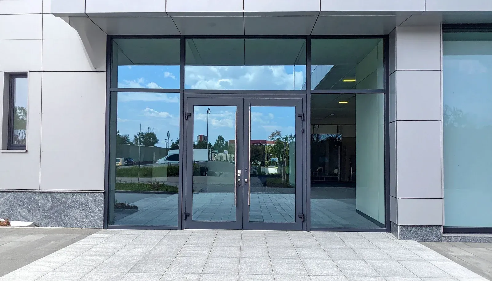 Glass entrance doors with surrounding windows. Gray building exterior, blue sky reflected in the glass.
