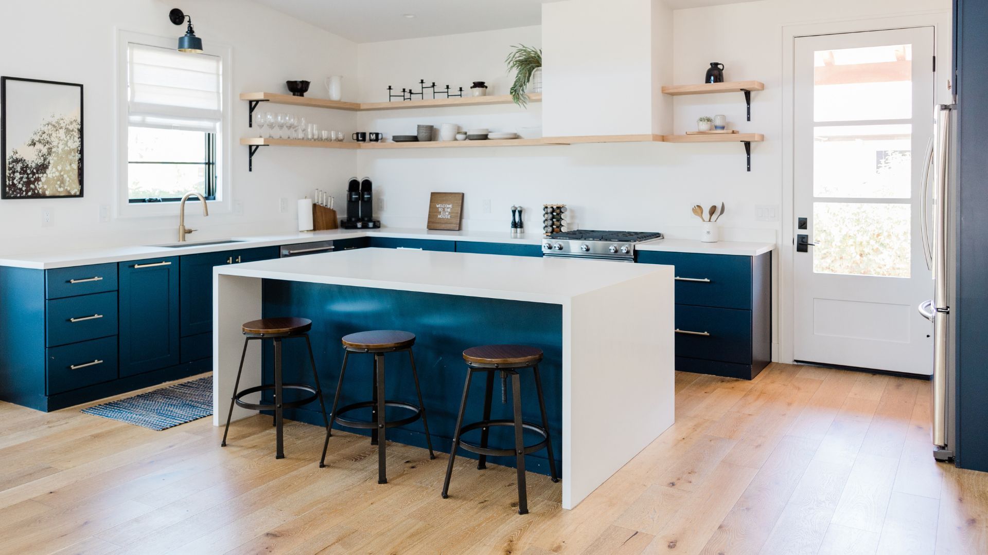 A kitchen with blue cabinets , white counter tops , and wooden floors.