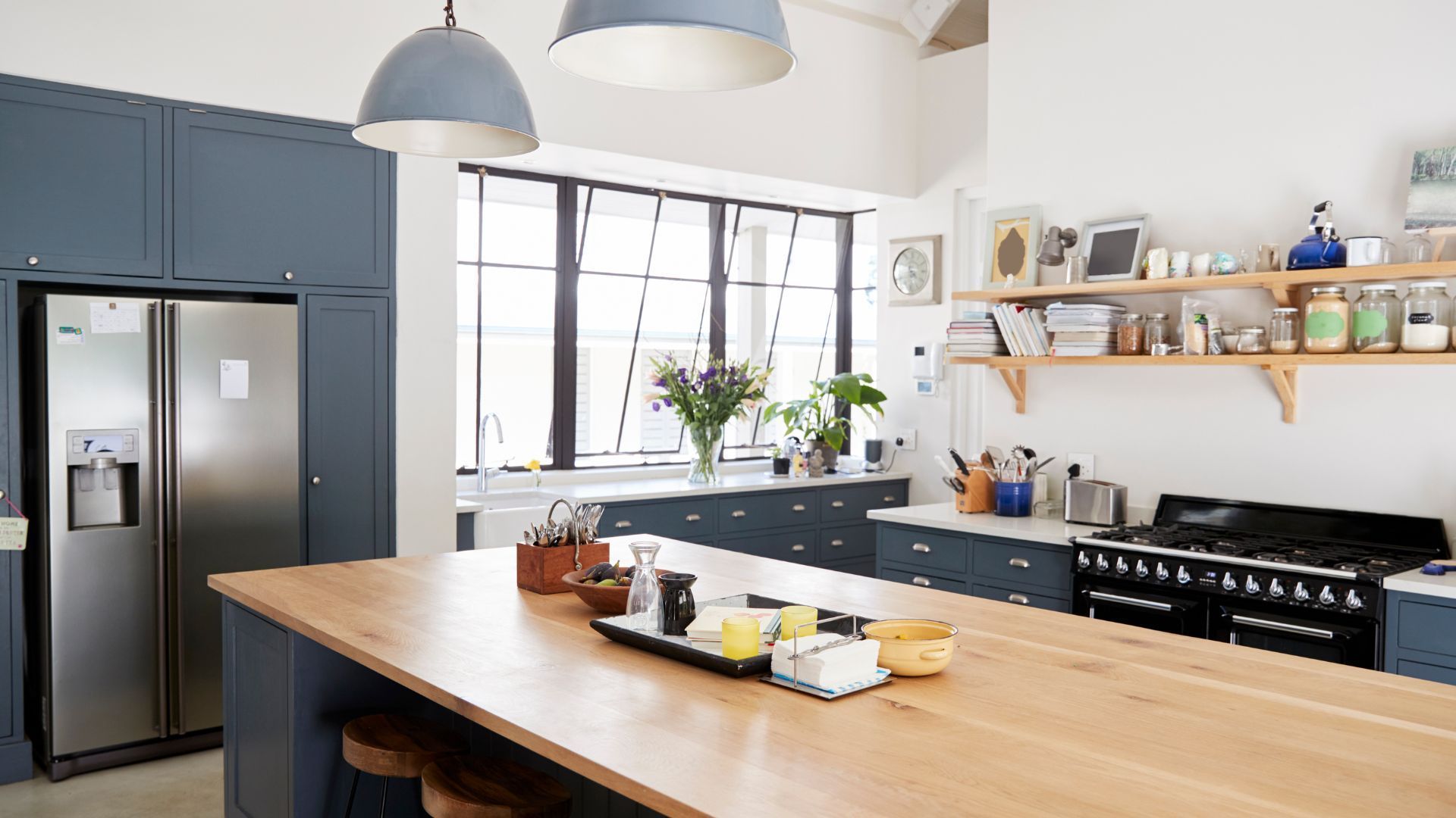 A kitchen with blue cabinets , a stainless steel refrigerator , a stove , and a wooden counter top.