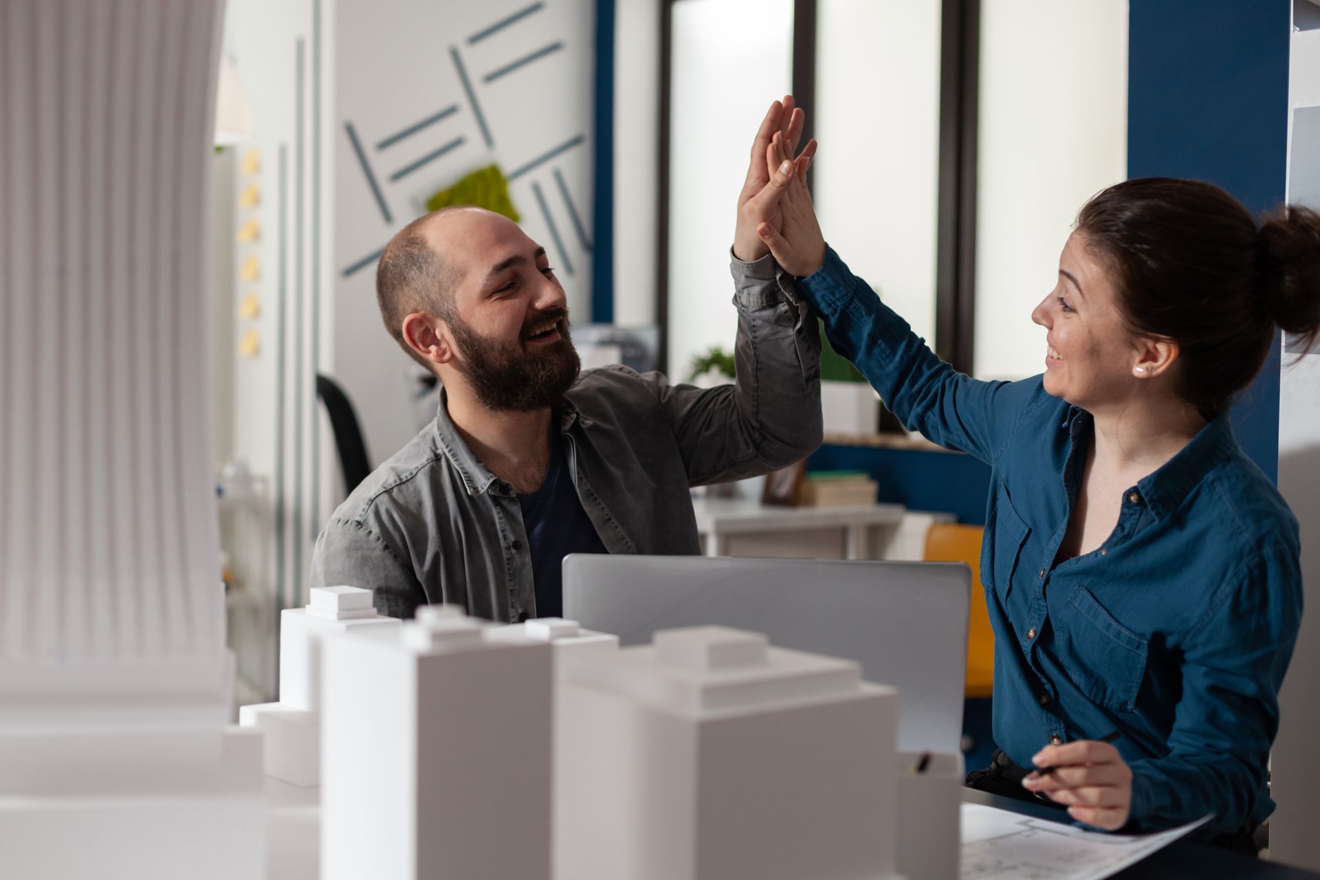 A man and a woman are giving each other a high five in an office.